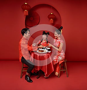 Asian family holding angpao gift in the meal on celebration chinese new year 2024 isolated on red backdrop.