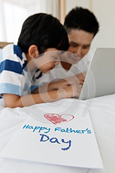 Asian family I love you, dad! Father and son together happy design a Father`s Day card with a computer on the bed at home.Concept