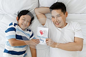 Asian family I love you, dad!The father and son were lying on the bed at home and showed the Father`s Day card that the son had