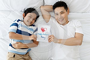 Asian family I love you, dad!The father and son were lying on the bed at home and showed the Father`s Day card that the son had