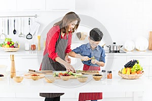 Asian family mom in red shirt and black apron is teaching her s