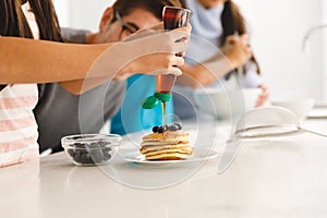 Asian family preparing breakfast in kitchen,father watching daughter put syrup on pancakes