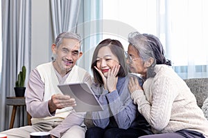 Asian family reunion of senior father mother and daughter sitting on couch with happy smile in retirement home while looking at