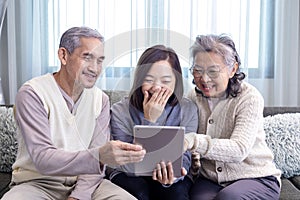 Asian family reunion of senior father, mother and daughter sitting on couch with happy smile in retirement home while looking at