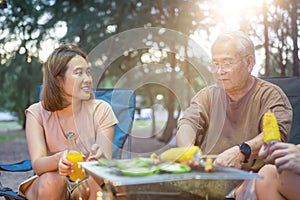 Asian family with senior drinking and having barbecue together. Cooking grilled bbq for dinner during camping on summer