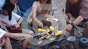 Asian family with senior drinking and having barbecue together. Cooking grilled bbq for dinner during camping on summer