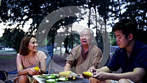 Asian family with senior drinking and having barbecue together. Cooking grilled bbq for dinner during camping on summer doliday