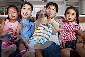 Asian Family Sitting On Sofa Watching TV Together