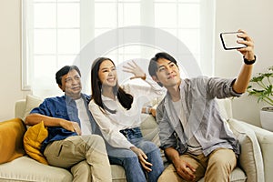 Asian family taking selfies happily lounging on the sofa in the living room.