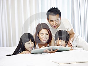 Asian family with two children reading book in bed