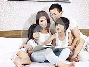 Asian family with two children reading book in bedroom