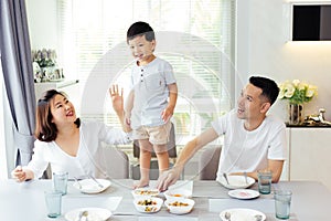Asian family watching their kid as he is determined and proud to finally stand on the dining table.