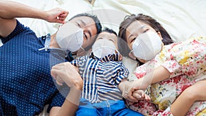 Asian family wearing protective visus Covid 19 and pm 2.5 N95 mask lying on white blanket