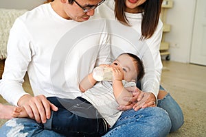 Asian family of young father and mother feeding a baby boy from milk bottle