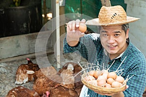 Asian farmers hold an eggs basket with their left hand and their right hand holding egg and holding up. At a chicken farm in their