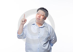 Asian Fat Man in blue shirt thinking and pointing to copyspace with doubts face isolated on white background.
