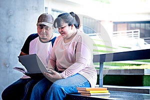 Asian fat woman and man student, sitting, looking and using computer notebook To review the lesson