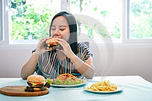 Asian fat woman sitting at the dining table I`m eating a hamburger.