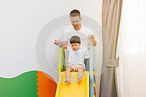 Asian father accompanying child on the playground slider at home. Happy family with toys.