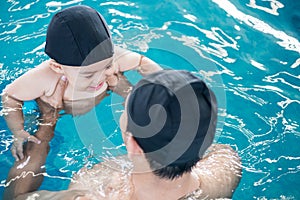 Asian father and baby lessons swimming pool in water