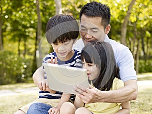 Asian father and children using tablet outdoors