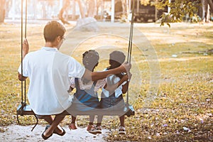 Asian father and daughter having fun to ride on swings together in playground