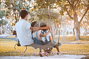 Asian father and daughter having fun to ride on swings together in playground