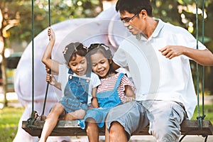 Asian father and daughter having fun to ride on swings together in playground