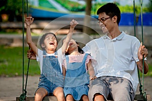 Asian father and daughter having fun to ride on swings together in playground