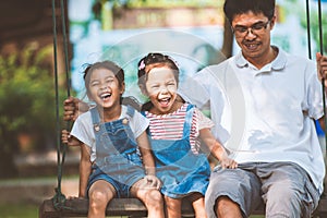 Asian father and daughter having fun to ride on swings together in playground