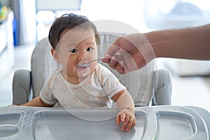 Asian father giving porridge to his kid on baby feeding seat.