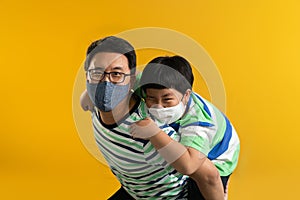 Asian father giving son ride on the back with a yellow background. Portrait of a happy father giving son piggyback a ride on his