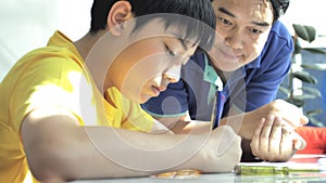 Asian father helping her son doing homework on white table