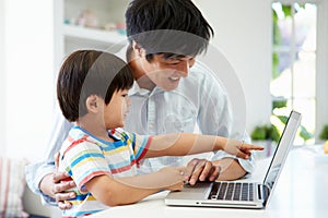 Asian Father Helping Son To Use Laptop At Home