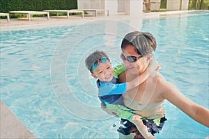 Asian Father holding cute little Asian toddler boy child at swimming pool in sunny day, Happy dad and son spending time together