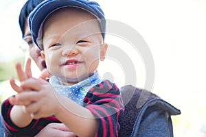 Asian Father holding Happy toddler baby boy smiling wearing sweater, bib, hat clapping hands at garden outdoors