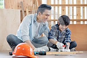 Asian father look carefully son use hammer to hopnailed in their workplace of carpentering with happy emotion. Asian family