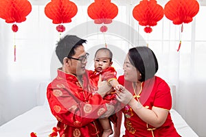 Asian father  mother hold son toddler boy on bed at home with love  Chinese new family in red Chinese costume give envelope to