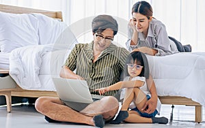 Asian Father, Mother, little daughter girl sitting in bedroom at home, using laptop, online studying, doing homework, watching