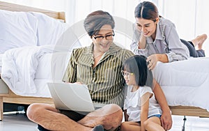 Asian Father, Mother, little daughter girl sitting in bedroom at home, using laptop, online studying, doing homework, watching