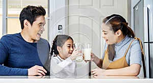 Asian Father, mother and little daughter spending time together and having breakfast drinking and hold glasses of milk at table