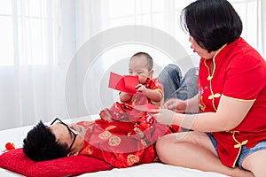 Asian father  mother playing with son toddler boy on bed at home  Chinese family in red Chinese costume give envelope to baby 
