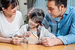 Asian Father and Mother teach young daughter to save money for future. Happy little girl enjoy put coins in piggy bank with