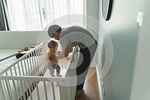 Asian Father putting his litte baby into crib in bedroom