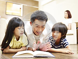 Asian father reading book telling story to two children