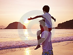 Asian father and son on beach at sunrise