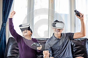 Asian father and son enjoy playing video games together with video joystick and Virtual Reality Glasses with exciting and very fun