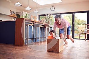 Asian Father And Son Pushing Son Around Kitchen Floor At Home In Junk Modelled Car