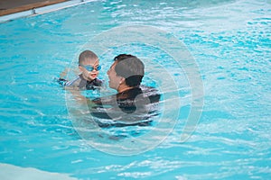 Asian Father and son takes a swimming lesson at swimming pool, Cute little Asian toddler boy child wearing swimming goggles