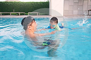 Asian Father and son takes a swimming lesson at swimming pool in sunny day - Selective focus at kid